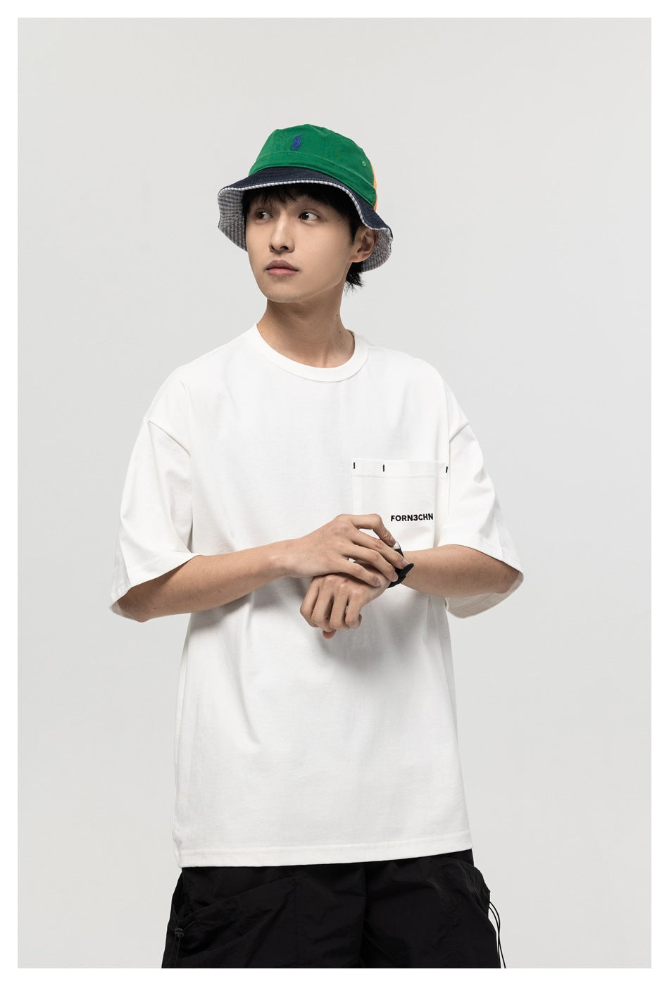 Model wearing a white oversized T-shirt with a stitched chest pocket and black text, shown from the front.