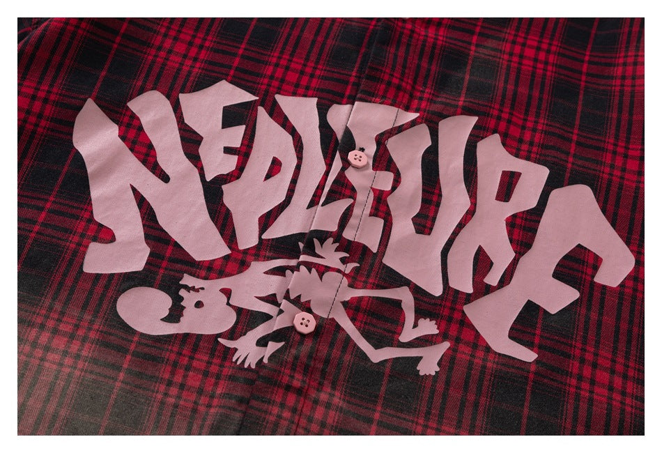 Close-up of a red-and-black plaid shirt with large pale graphic lettering and an illustrated figure.