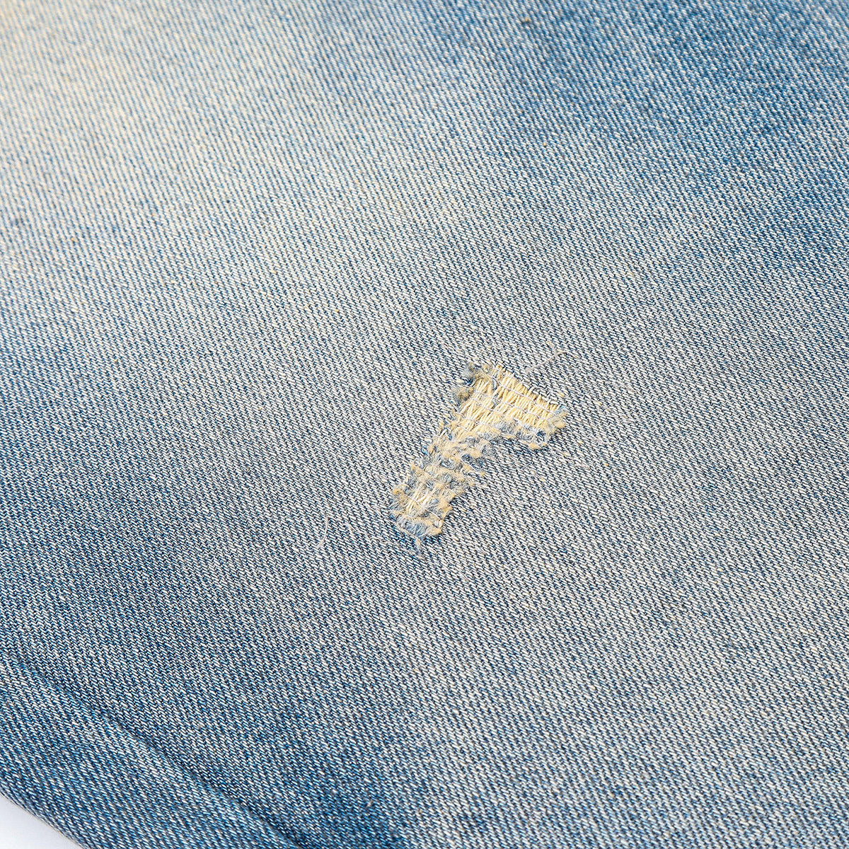 Close-up of light blue denim with a small stitched repair or distressed patch.