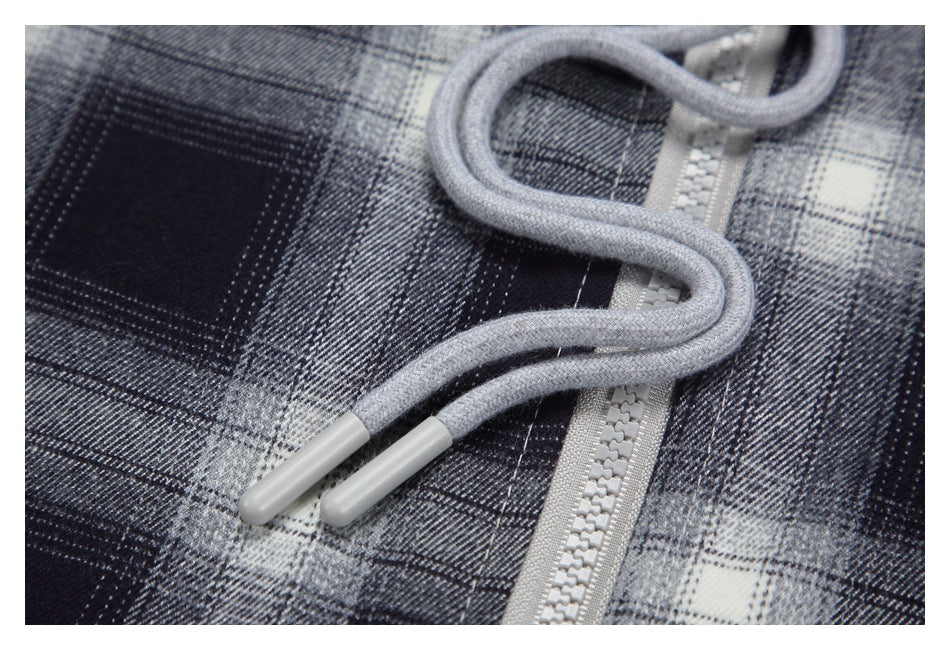 Close-up of gray drawstrings and a light gray zipper on a black, gray, and white plaid hoodie.
