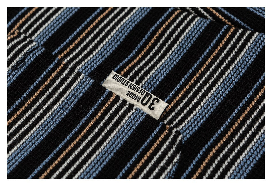 Close-up of black knit fabric with blue, cream, and tan stripes and a small sewn white label.