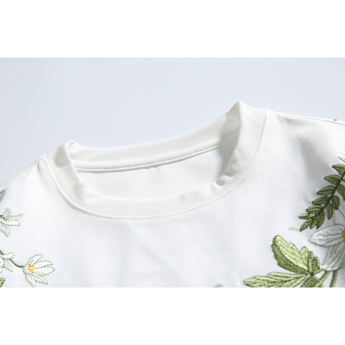 Close-up of a white T-shirt's ribbed crew neck and partial green botanical embroidery.