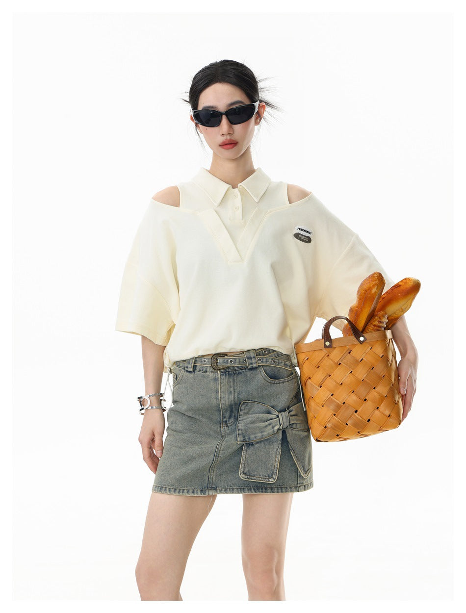 Close view of a model in a cream cropped polo top with cold-shoulder cutouts and denim skirt, carrying a woven basket