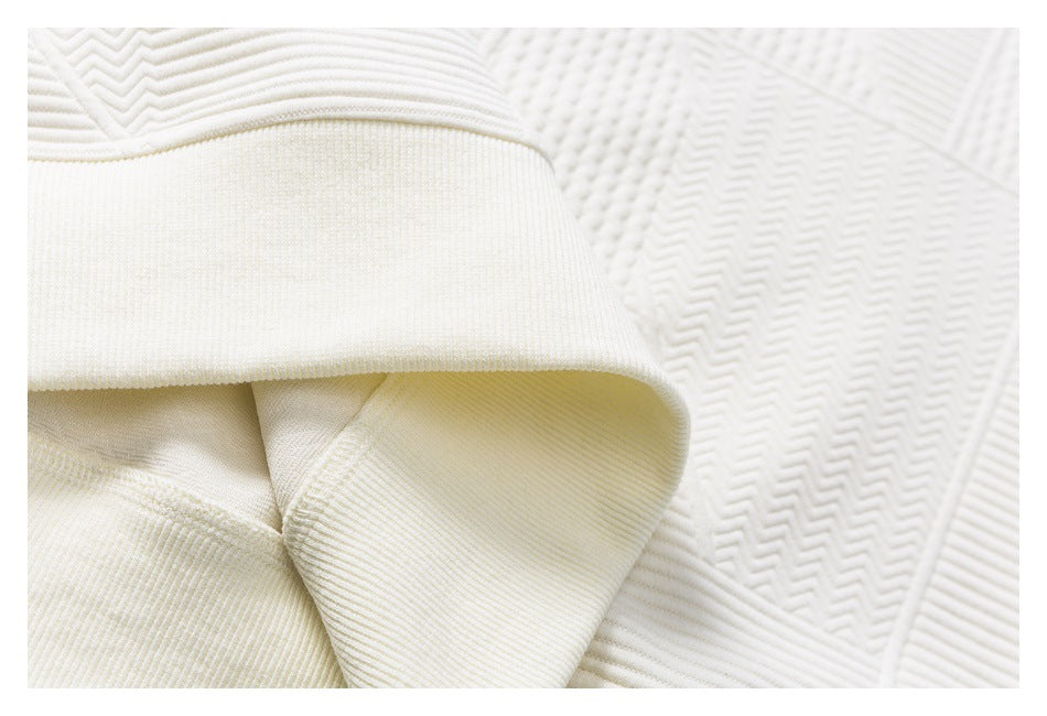 Close-up of a wide cream ribbed cuff and seam against patterned quilted fabric.