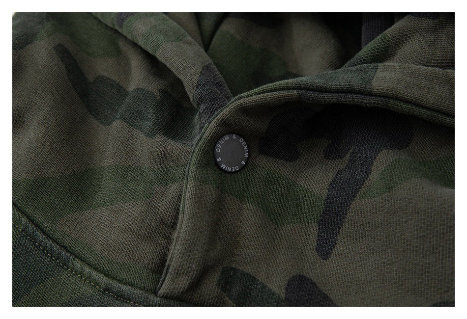 Close-up of a dark green camouflage garment with a black snap button and stitched seam.