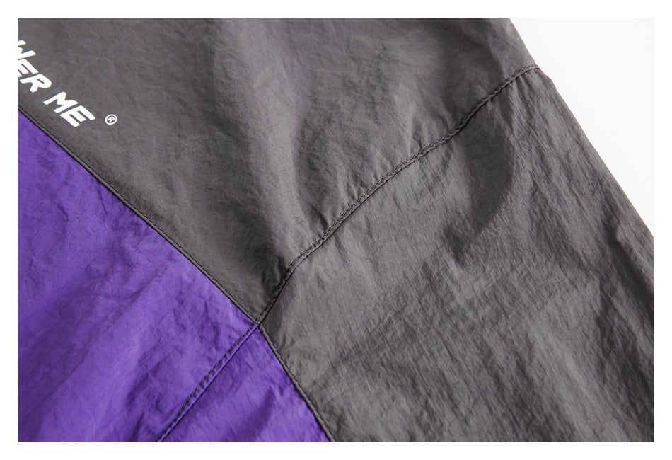 Close-up of a charcoal and purple jacket panel seam with partial white garment lettering.