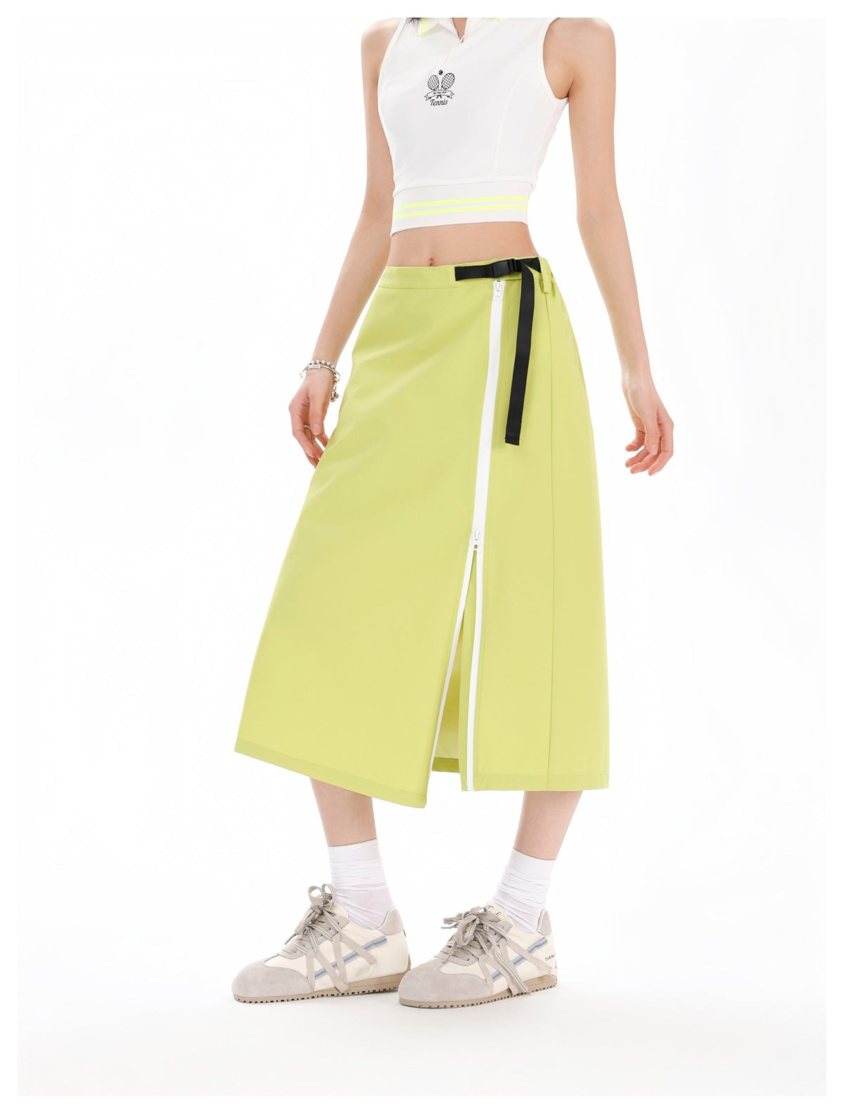 Model wearing a lime-green midi skirt with a long white front-side zipper and black belt detail, paired with a white cropped