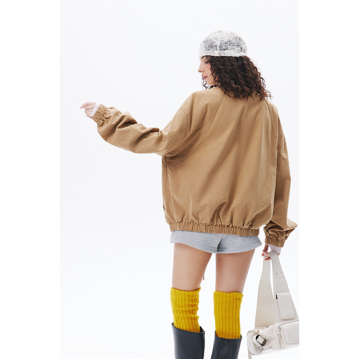 Rear view of a model wearing an oversized tan jacket with an elastic hem and cuffs, gray shorts and yellow socks.