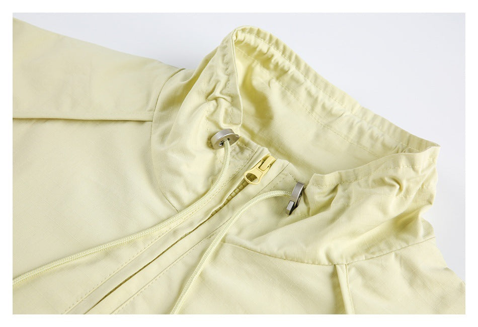 Pale yellow garment waist detail with a button tab, zipper and drawcords.