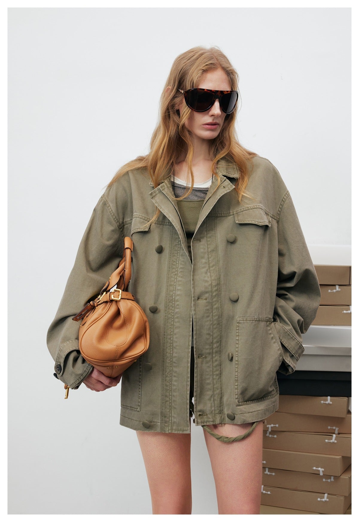 Close view of a model wearing an oversized olive utility jacket with a pointed collar, flap pockets and a button front.