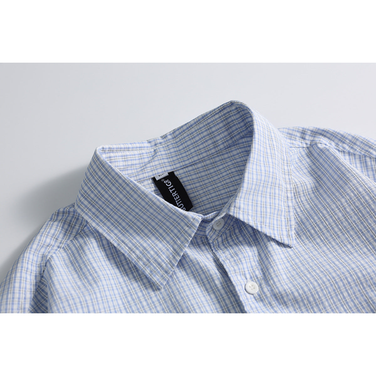Close-up of a light blue and white checked shirt collar, placket, and black neck label.