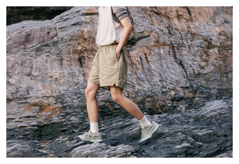Side view of a model walking in tan drawstring shorts with side pockets on rocky terrain.