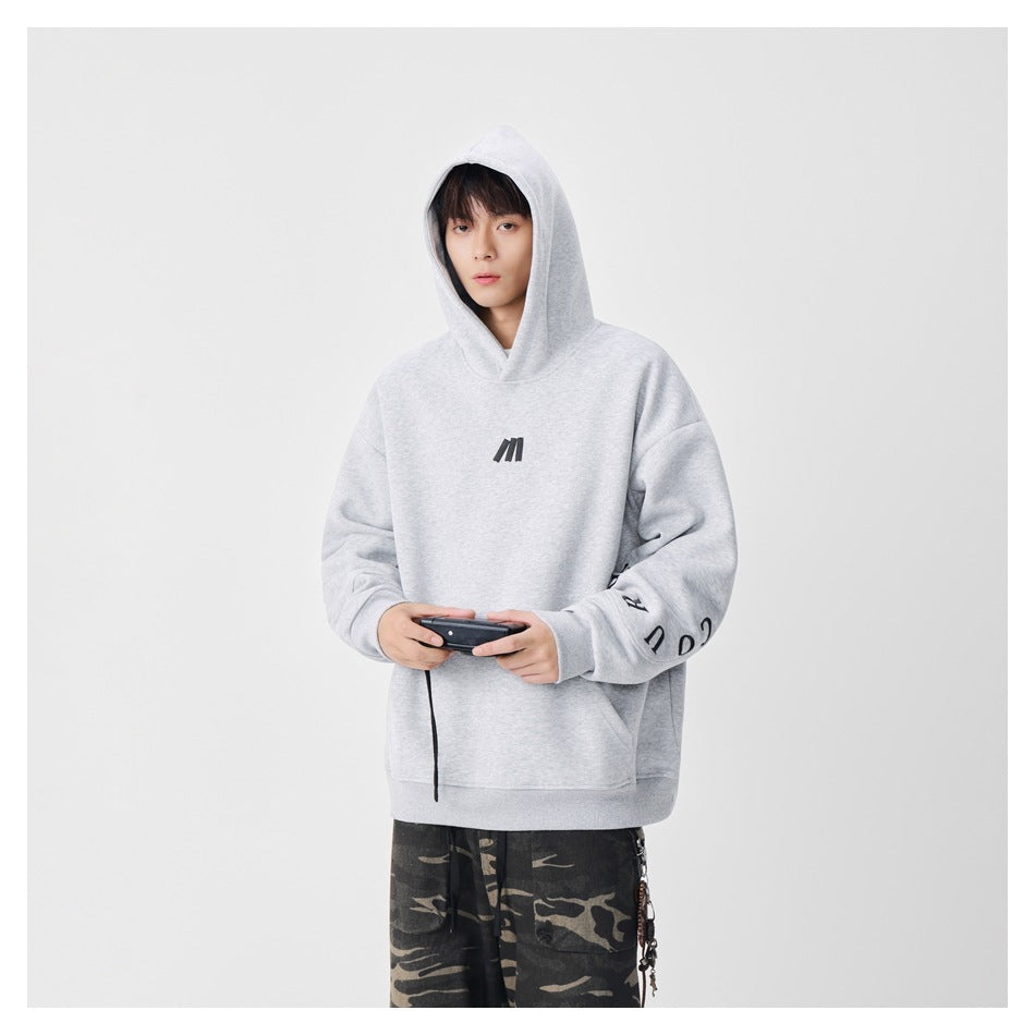 Model wearing a light gray hooded sweatshirt with a small black chest emblem and sleeve lettering.