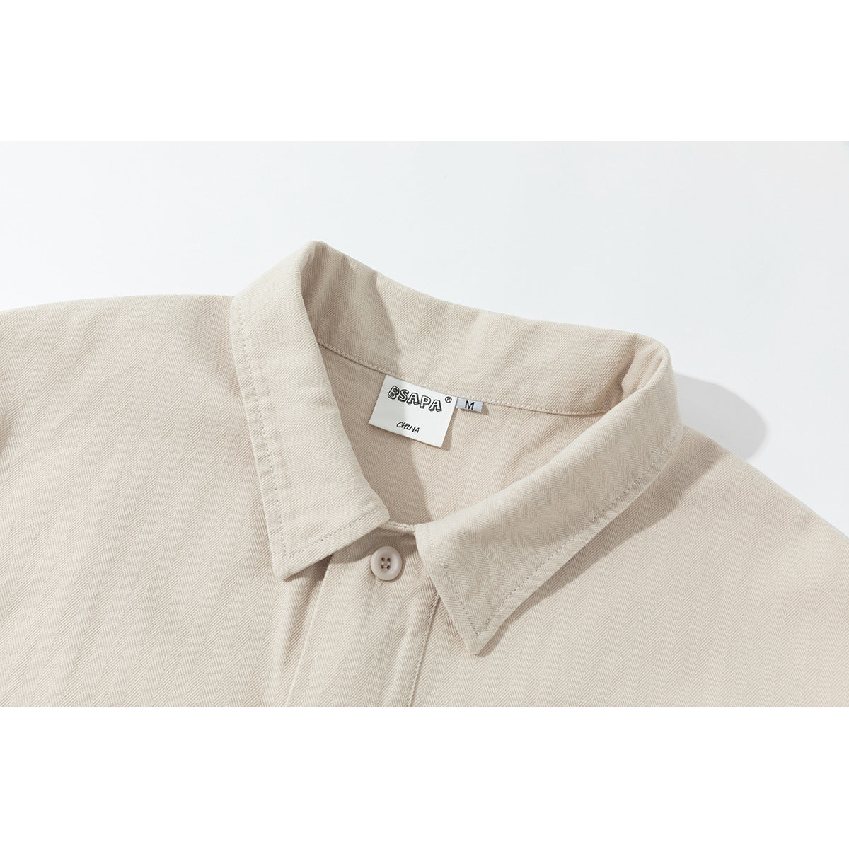 Close-up of a cream herringbone shirt collar, top button, and sewn neck label.