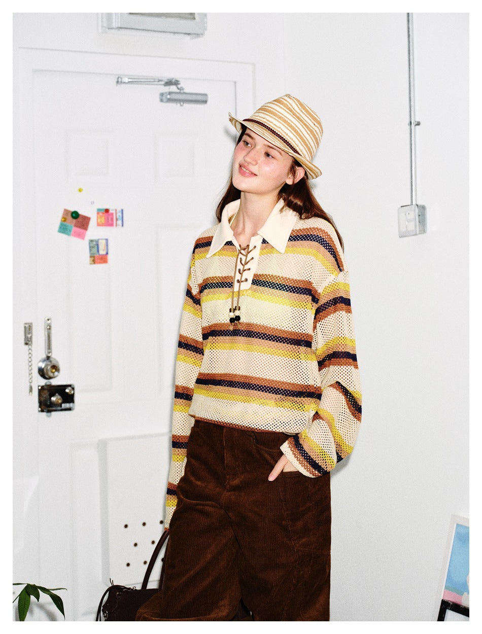 Model wearing a striped cream mesh rugby shirt with a pointed collar and lace-up placket, shown with brown trousers.