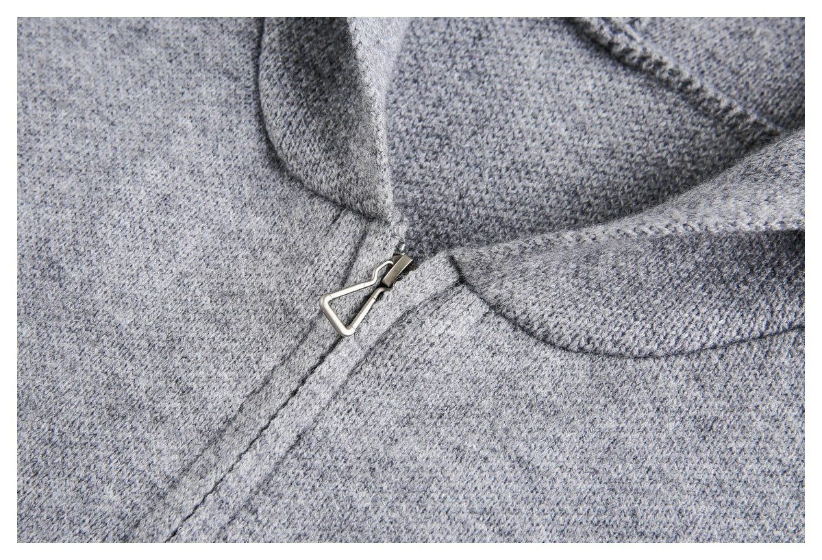 Close-up of gray knit fabric with a metal zipper pull beside a folded, curved edge.