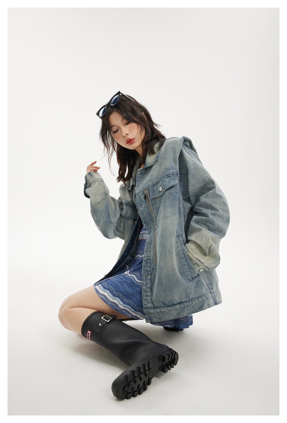 Model seated in an oversized light-wash denim jacket with zip details and flap pockets.