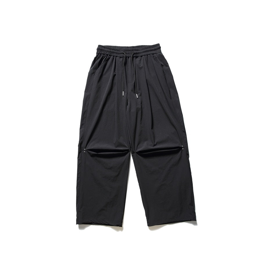 Black wide-leg drawstring pants with knee pleats and snap details, flat lay on a white background