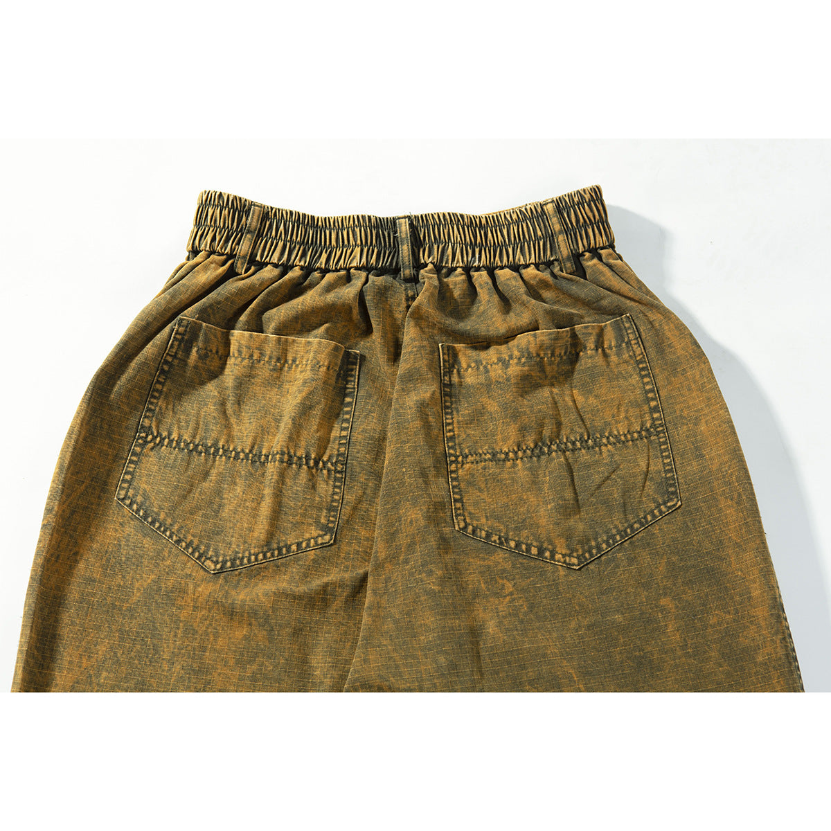 Rear close-up of ochre-brown trousers with a gathered elastic waistband and two large patch pockets.