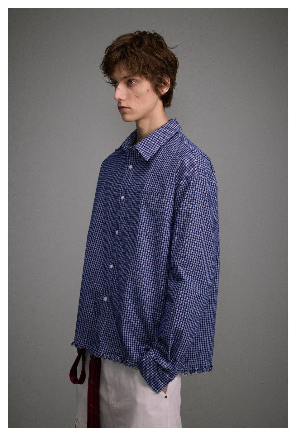 Side view of a model wearing a blue small-check button-up shirt with a frayed hem and white cargo pants.