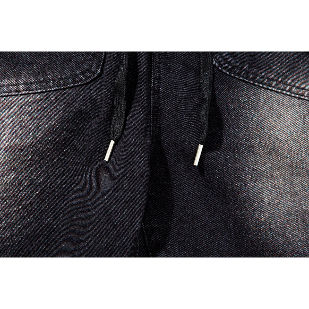 Close-up of black shorts with two black drawstrings ending in silver-colored tips.
