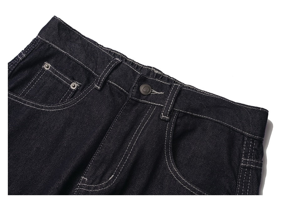 Close-up of black denim jeans showing the waistband, button, belt loops, and front pockets with contrast stitching.