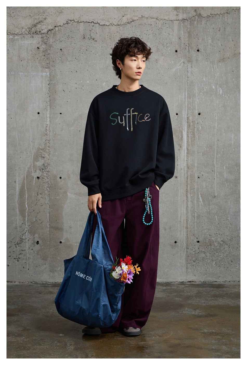 Full-length model wearing a black sweatshirt with colorful chest lettering and loose burgundy pants.