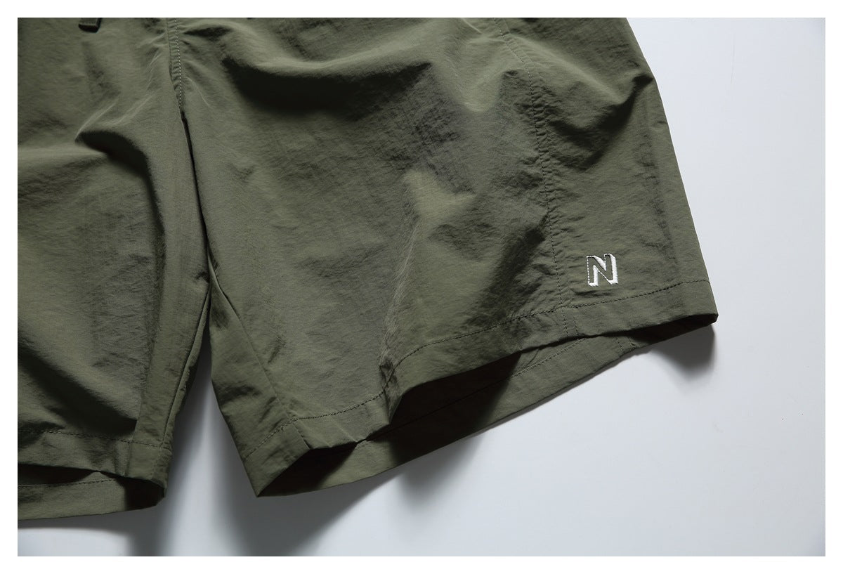 Close-up of the olive shorts' leg hem with a small white embroidered N.