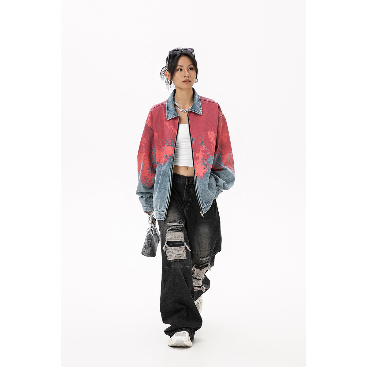 Model wearing an oversized blue denim zip jacket with coral-red mottled detailing and black ripped jeans, front view.