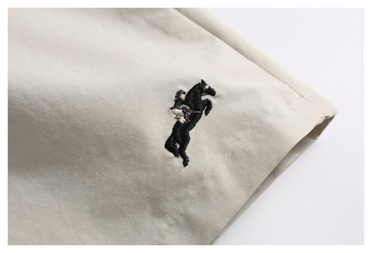 Close-up of a small embroidered black horse and rider on light beige shorts.