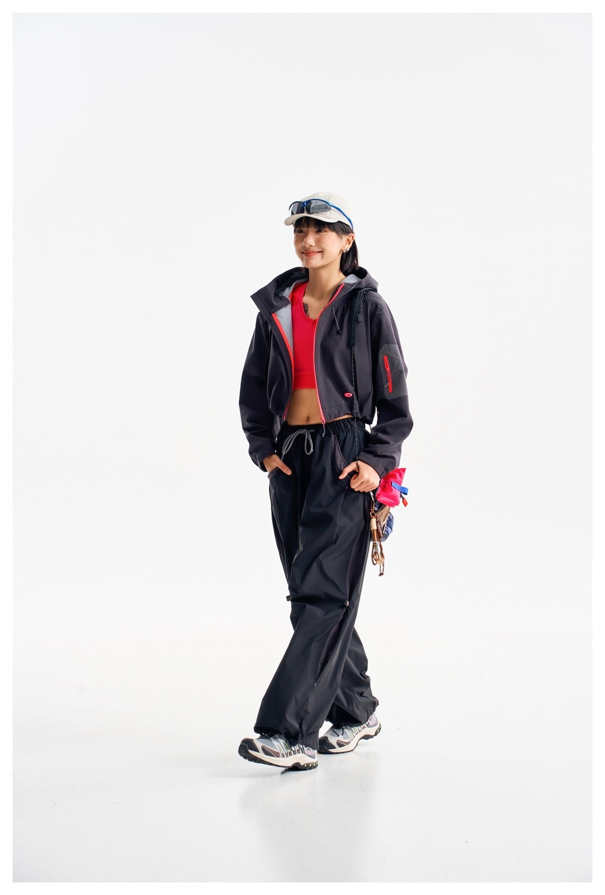 Model walking in a dark cropped hooded jacket with vivid pink trim and loose dark pants.