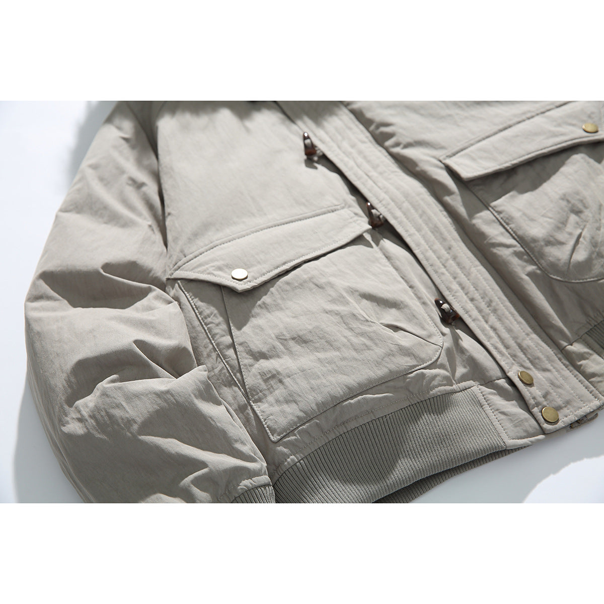 Close-up of a light gray jacket showing flap pockets, toggle closures, and front snaps.