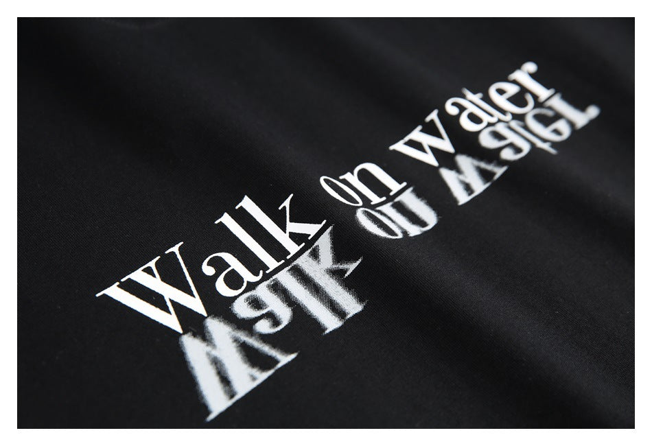 Angled close-up of white “Walk on water” lettering with a mirrored reflection effect on black fabric.