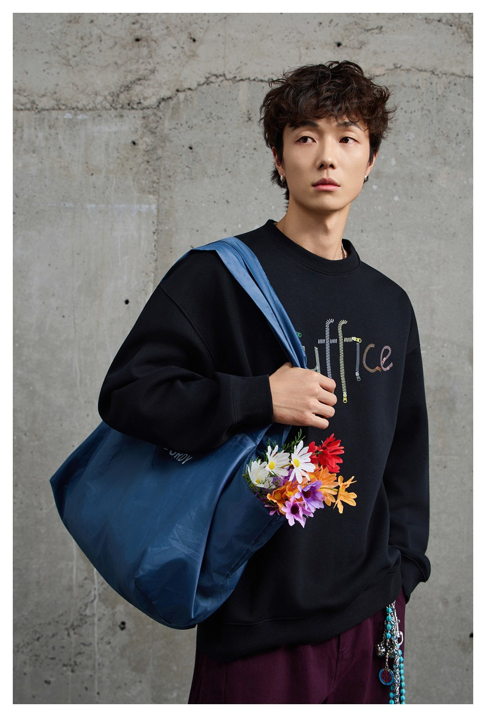 Model wearing a black crewneck sweatshirt with colorful embroidered lettering and flowers on the front.