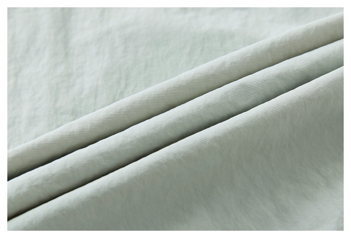 Close-up of pale sage-gray pants fabric folded into layers, showing its fine surface texture.