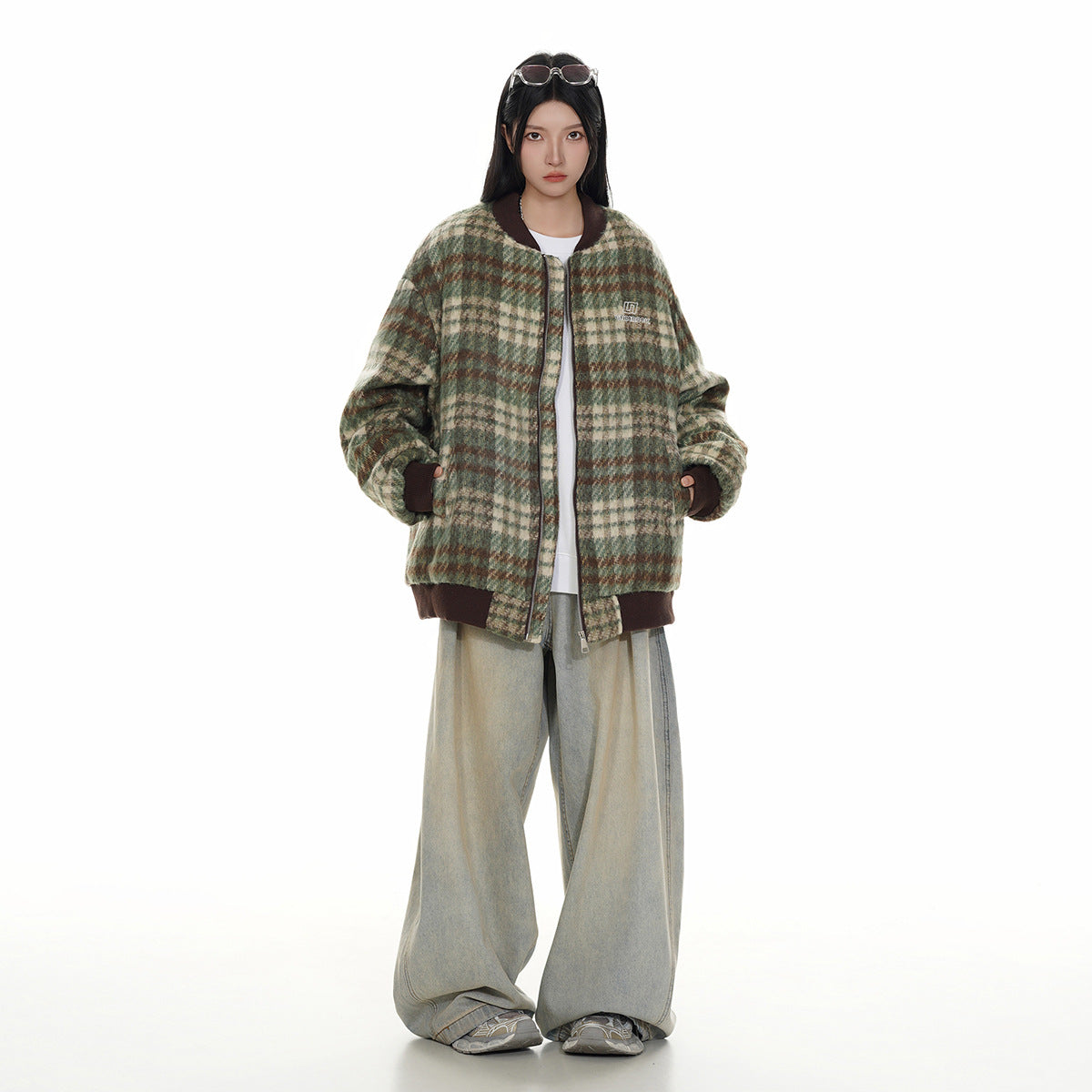 Full-length front view of a model wearing a green plaid zip jacket with dark brown trim and loose light jeans.