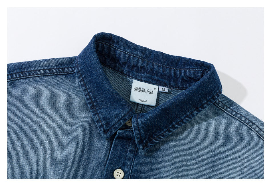 Close-up of a blue denim shirt collar and upper placket with a visible neck label and white button.