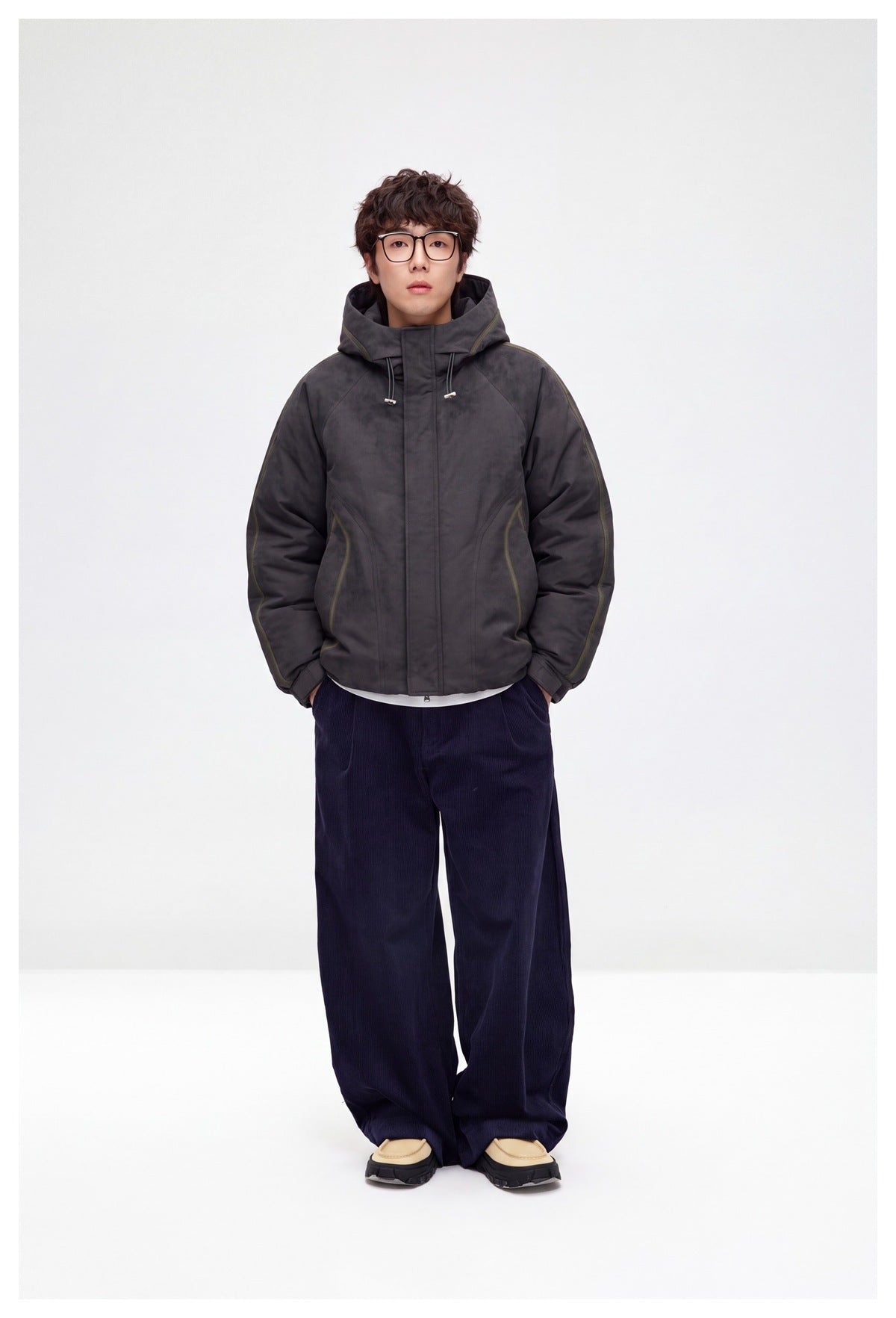Full-length view of a model in a dark gray hooded jacket, navy wide-leg corduroy pants and beige shoes