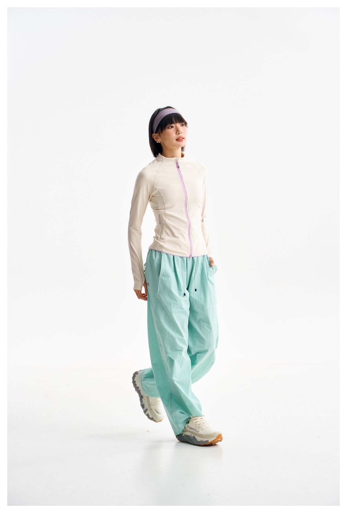 Full-length model wearing an ivory zip-front jacket with lavender trim and loose mint-green trousers.