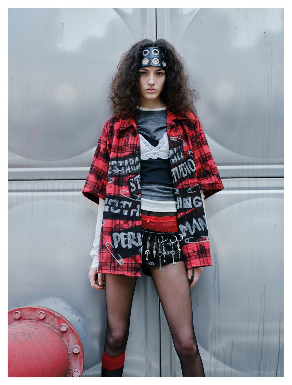 Closer view of a model wearing the red-and-black plaid graphic shirt over layered tops, with black shorts and dangling