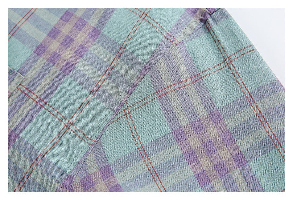 Close-up of a stitched seam on a mint and lavender plaid shirt with thin rust-red lines.