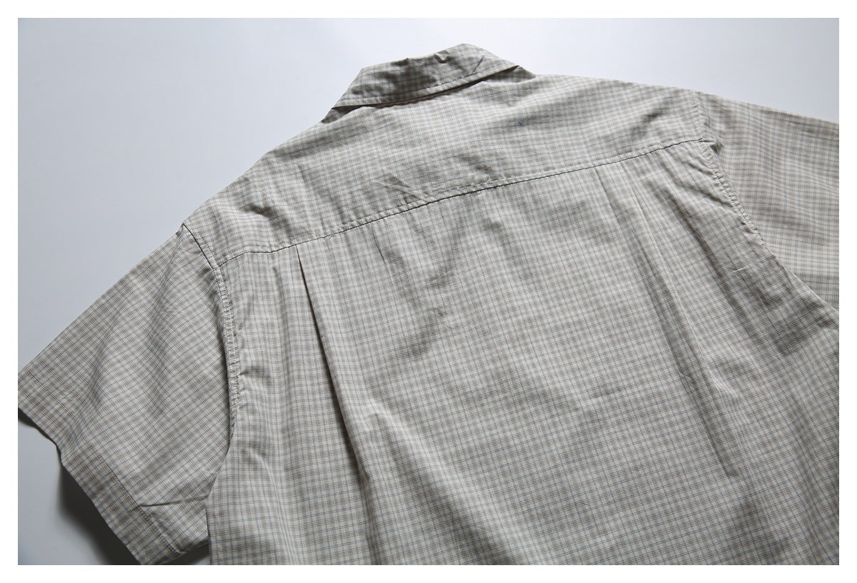 Partial back view of a beige plaid shirt laid flat, showing the collar, yoke and short sleeves.