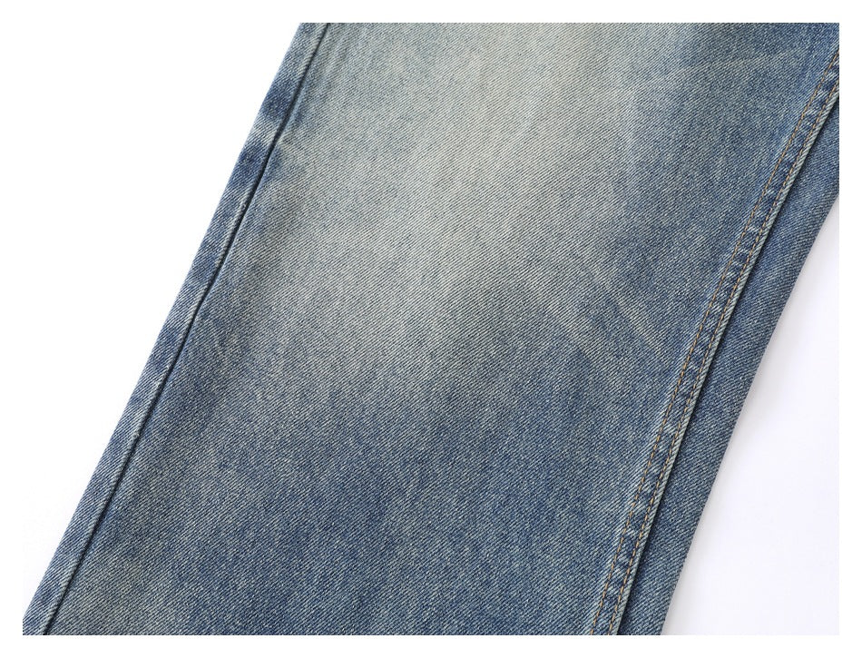 Close-up of a blue faded denim trouser leg with a diagonal seam and tan stitching.