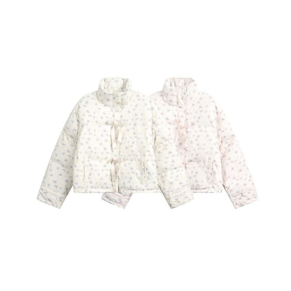 Two puffer jackets shown together in pale cream and blush pink, both with small floral prints and front ribbon ties.