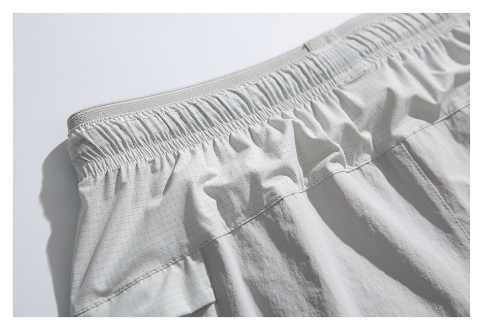 Angled close-up of pale gray shorts with a gathered elastic waistband, subtle grid pattern, and stitched seams.