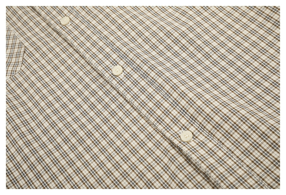 Close-up of the beige and brown checked shirt's button placket with cream buttons.