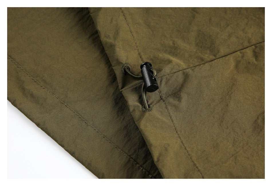 Close-up of olive-brown garment fabric with a black cord toggle and stitched seams.