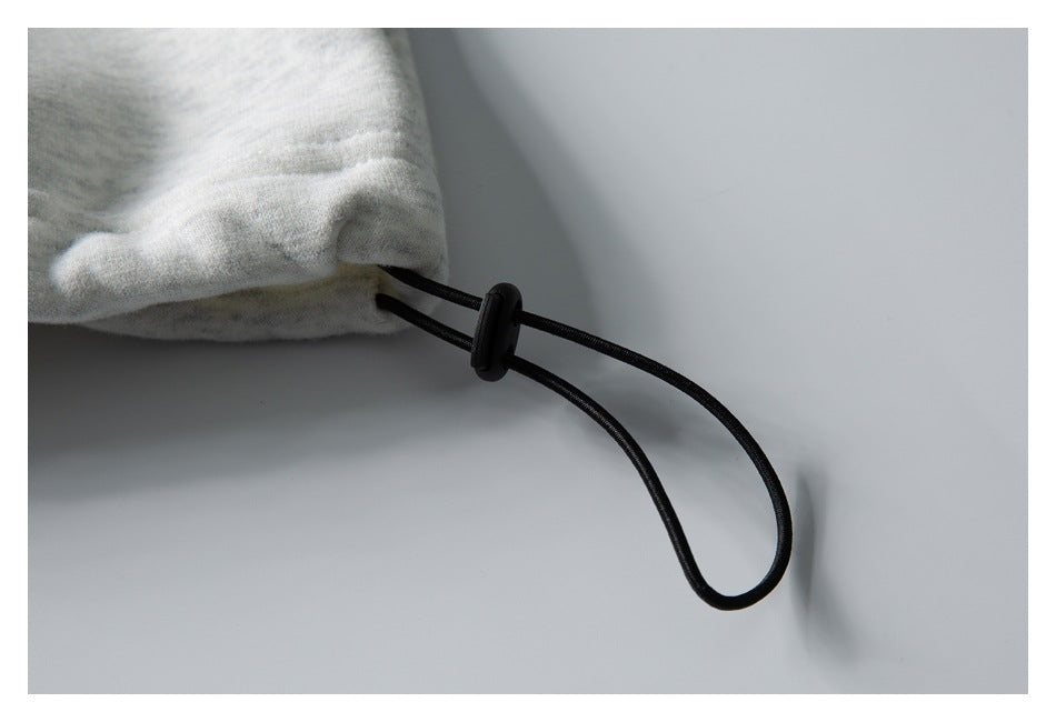 Close-up of a black drawcord and slider attached to the gathered edge of a light gray heather garment.
