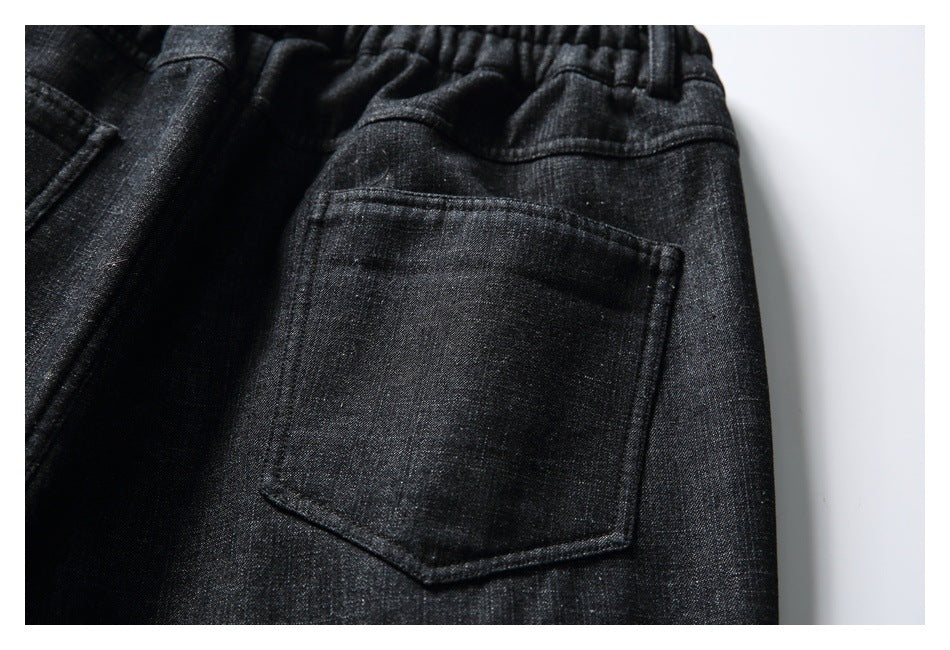 Close-up of a back patch pocket and gathered waistband on black textured trousers.