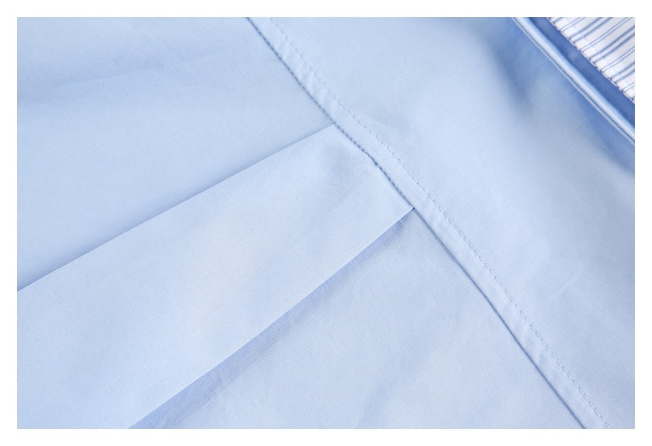Close-up of a pale blue shirt pocket and stitched panel, with a glimpse of striped trim.